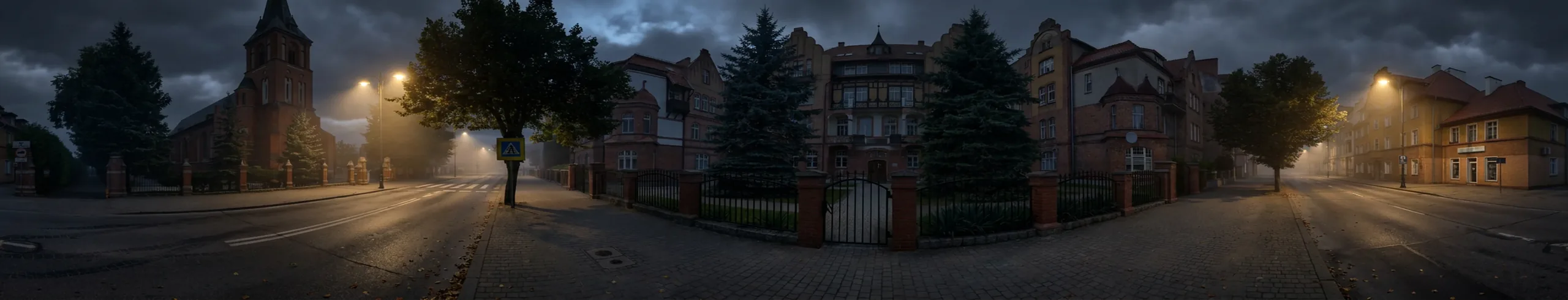 Nocna ulica w Ełku z wieżą kościoła i kamienicami za ogrodzeniem